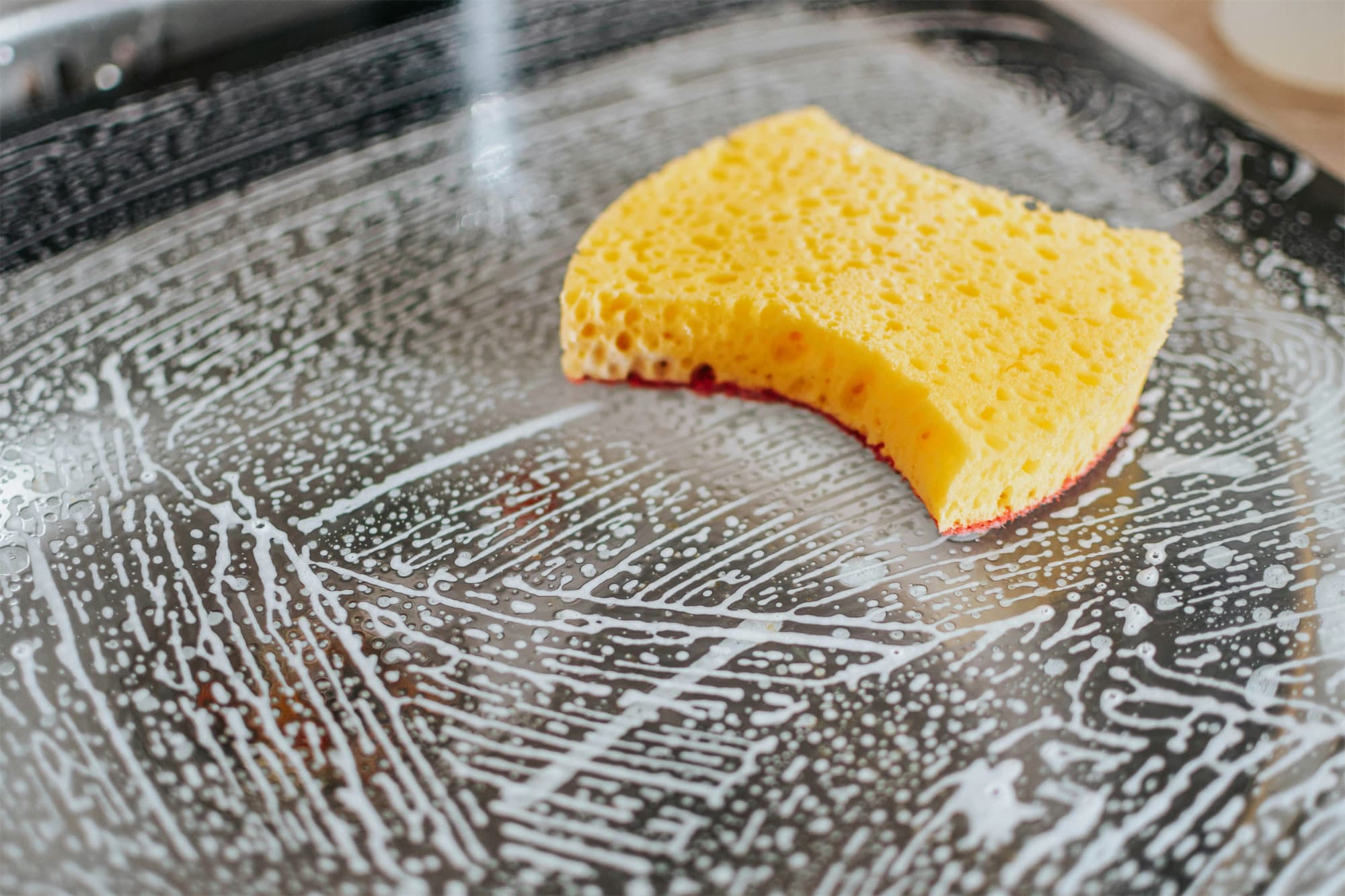 Fresh soap suds and a yellow sponge on a dark cooktop